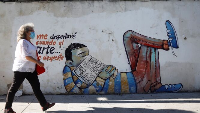 Una mujer protegida con mascarilla  pasa junto a un graffiti por las calles de Córdoba